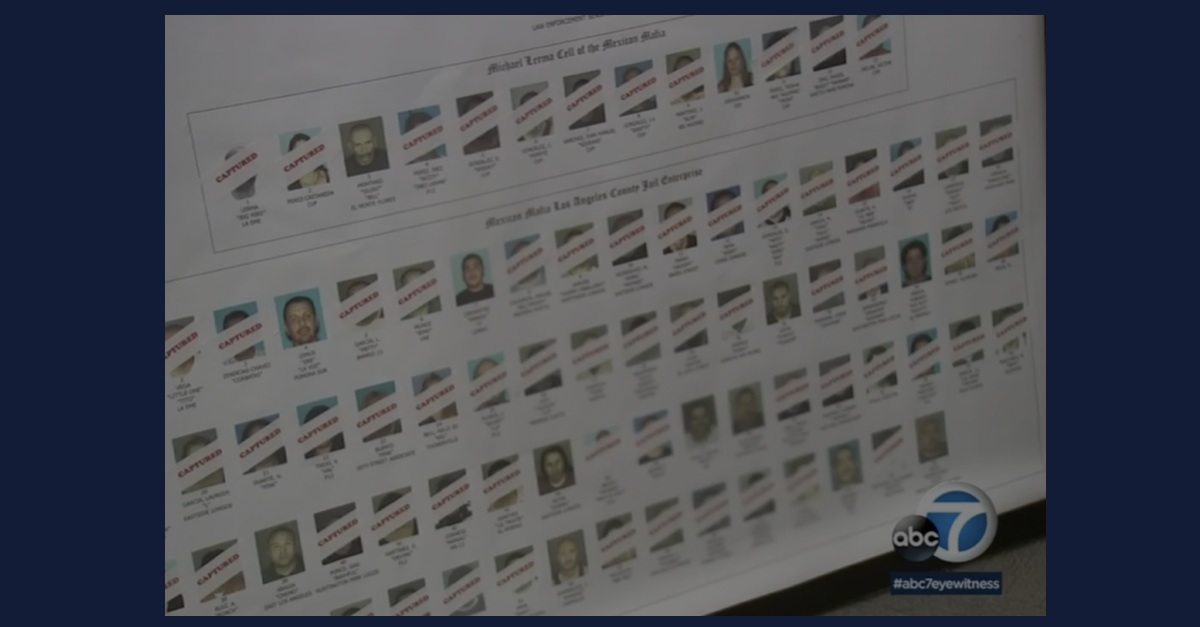 A screenshot showing a large poster of mugshots displayed during a 2018 press conference about federal indictments targeting the Mexican Mafia