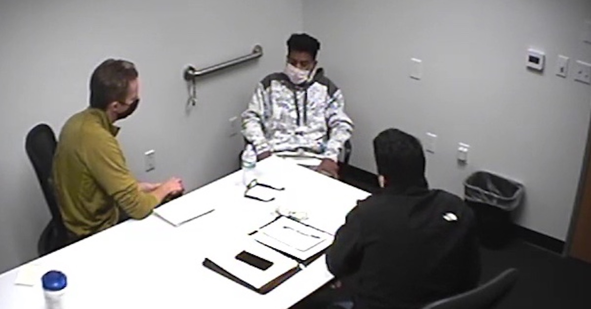 Daniel Rodriguez, with dark hair and a mask over his face, sits at the corner of a table facing two federal investigators. He is wearing a gray sweatshirt.